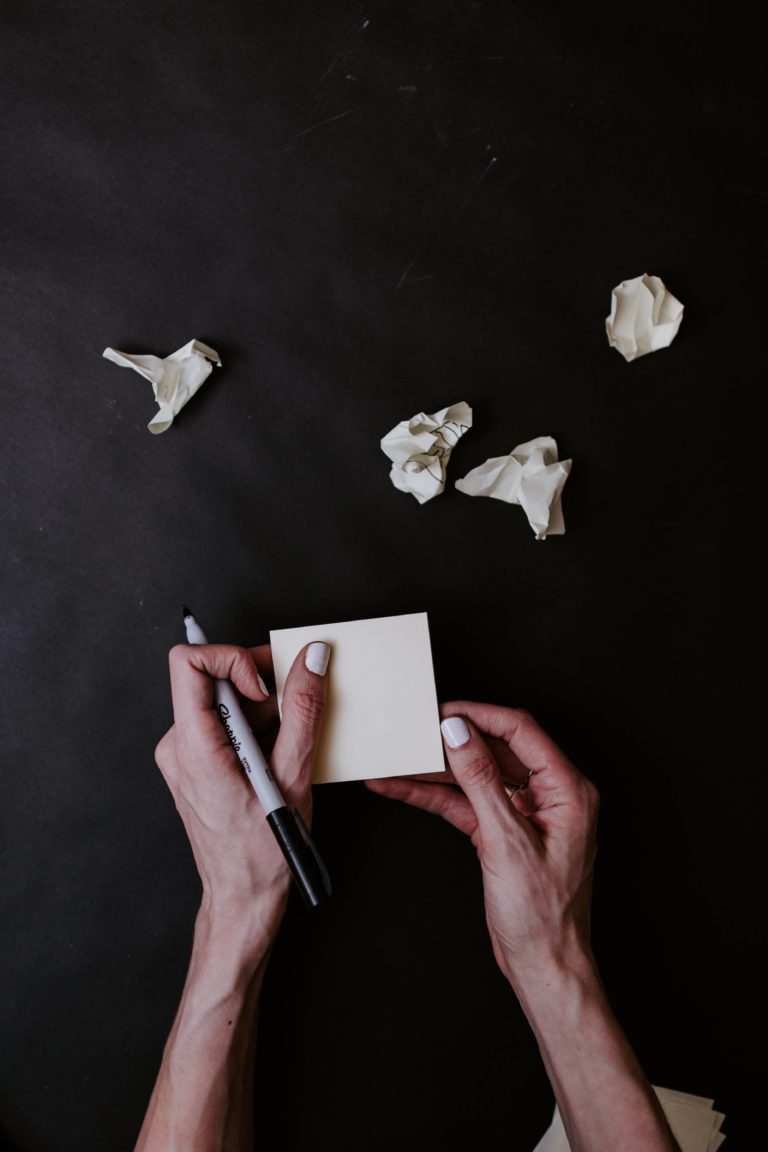 girl is holding marker writing on a sticky not after mistakes or mess ups shown by the crumpled paper on the table